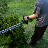 Person using a hedge trimmer to trim a bush outdoors.
