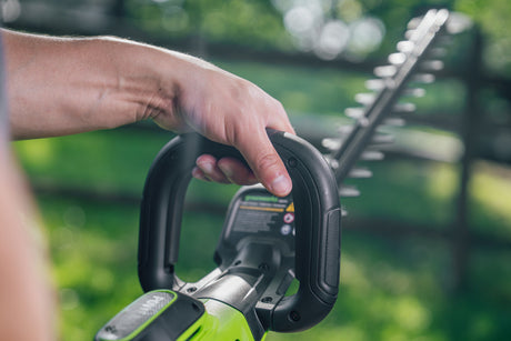 Hand holding a cordless hedge trimmer with a blurred green background